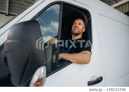 Sitting in a van and smiling. Courier of delivery service company is at work Sitting in a van and smiling. Courier of delivery service company is at work 139231398