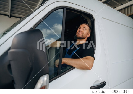 Sitting in a van and smiling. Courier of delivery service company is at work Sitting in a van and smiling. Courier of delivery service company is at work 139231399