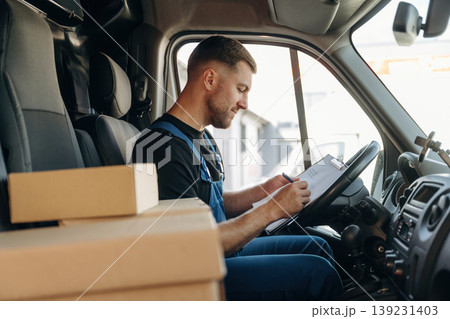Fills out the document, writes on the invoice. Inside of the bus with delivery service man in uniform Fills out the document, writes on the invoice. Inside of the bus with delivery service man in uniform 139231403
