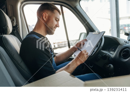 Fills out the document, writes on the invoice. Inside of the bus with delivery service man in uniform Fills out the document, writes on the invoice. Inside of the bus with delivery service man in uniform 139231411
