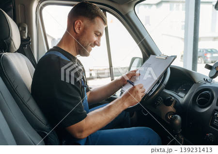 Fills out the document, writes on the invoice. Inside of the bus with delivery service man in uniform 139231413