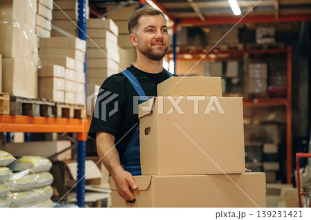 Walking and holding the boxes. Man in uniform is working in the storage with packages for shipment 139231421
