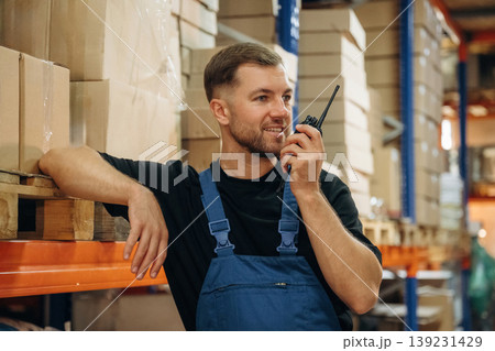 Conversation by using walkie talkie. Man in uniform is working in the storage with packages for shipment Conversation by using walkie talkie. Man in uniform is working in the storage with packages for shipment 139231429