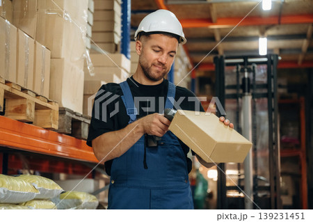 Boxes are getting scanned. Man in uniform is working in the storage with packages for shipment 139231451