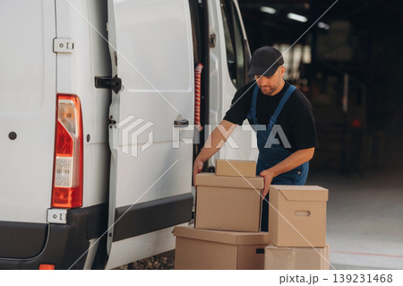 A lot of boxes. Delivery man is by the bus near garage outdoors A lot of boxes. Delivery man is by the bus near garage outdoors 139231468