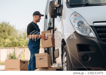 Male courier is near the van, holding the packages Male courier is near the van, holding the packages 139231475