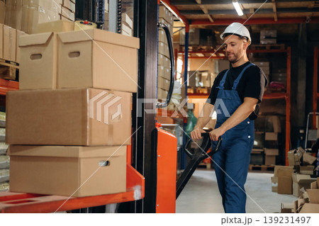 Transporting the boxes by using forklift. Man in uniform is working in the storage with packages for shipment 139231497