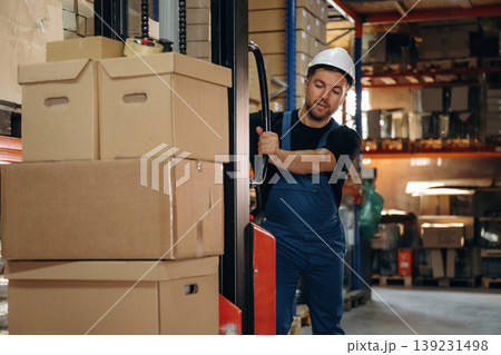 Transporting the boxes by using forklift. Man in uniform is working in the storage with packages for shipment 139231498