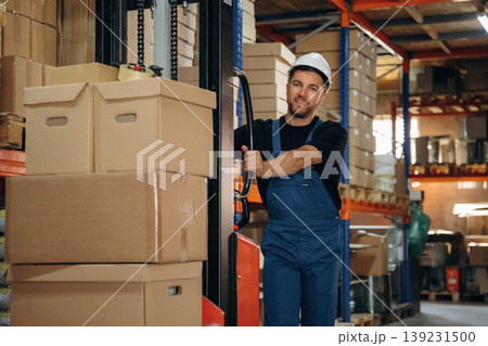 Preparing boxes for shipment by moving them by forklift. Man in uniform is working in the storage Preparing boxes for shipment by moving them by forklift. Man in uniform is working in the storage 139231500