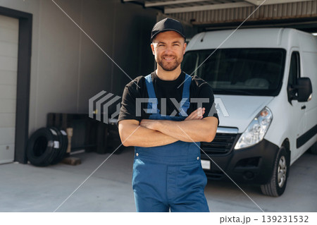 Arms crossed, standing. Delivery man is by the bus near garage outdoors Arms crossed, standing. Delivery man is by the bus near garage outdoors 139231532