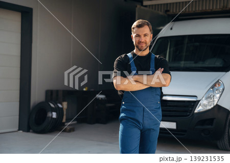 Arms crossed, standing. Delivery man is by the bus near garage outdoors 139231535