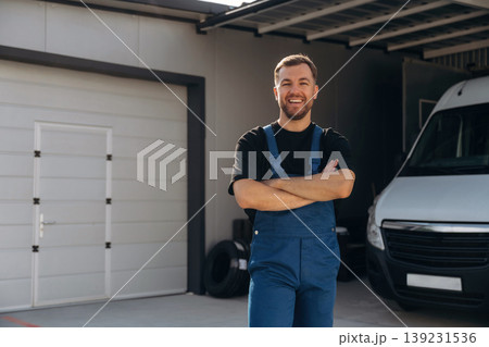 Arms crossed, standing. Delivery man is by the bus near garage outdoors 139231536