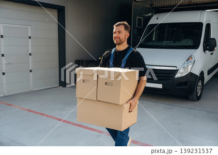 The boxes are in hands. Delivery man is by the bus near garage outdoors The boxes are in hands. Delivery man is by the bus near garage outdoors 139231537