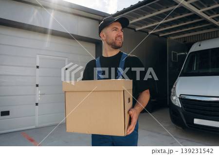 Paper box in hands. Delivery man is by the bus near garage outdoors 139231542