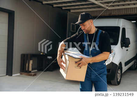 Data in the notepad, holding box. Delivery man is by the bus near garage outdoors Data in the notepad, holding box. Delivery man is by the bus near garage outdoors 139231549