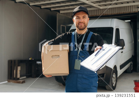 Data in the notepad, holding box. Delivery man is by the bus near garage outdoors Data in the notepad, holding box. Delivery man is by the bus near garage outdoors 139231551
