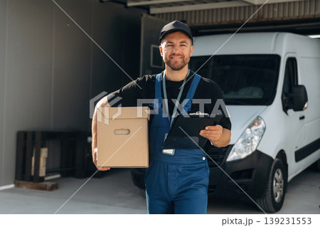 Data in the notepad, holding box. Delivery man is by the bus near garage outdoors Data in the notepad, holding box. Delivery man is by the bus near garage outdoors 139231553