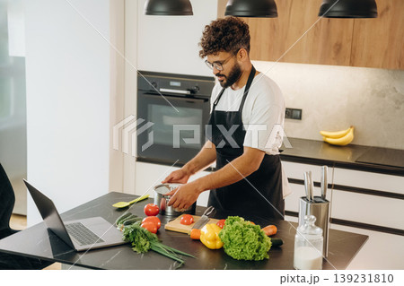In black apron. Handsome man is preparing food on the kitchen In black apron. Handsome man is preparing food on the kitchen 139231810