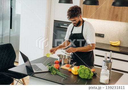 In black apron. Handsome man is preparing food on the kitchen In black apron. Handsome man is preparing food on the kitchen 139231811