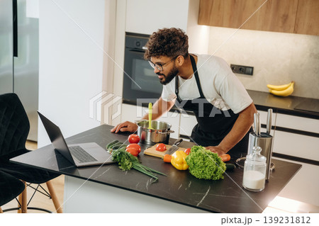 In black apron. Handsome man is preparing food on the kitchen In black apron. Handsome man is preparing food on the kitchen 139231812
