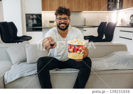 Popcorn and TV controller. Man is in the modern domestic room at home Popcorn and TV controller. Man is in the modern domestic room at home 139231838