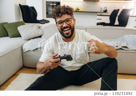 Celebrating victory, playing video game by using controller. Man is in the modern domestic room at home 139231892