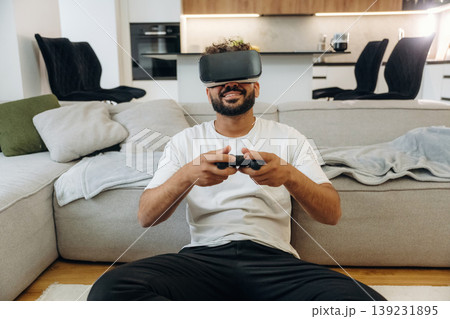 Virtual reality glasses, controller in hands. Man is in the modern domestic room at home Virtual reality glasses, controller in hands. Man is in the modern domestic room at home 139231895
