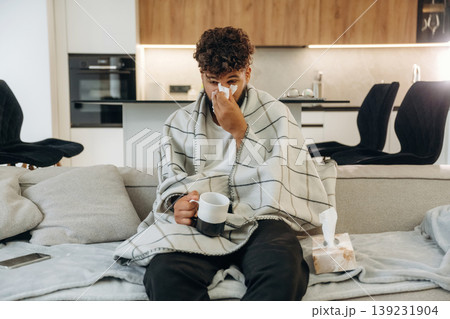 Warm tea in the cup. Sick man is on the sofa at home, with towel, feeling bad 139231904