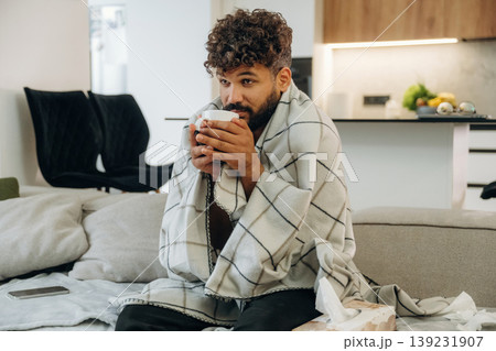 Warm tea in the cup. Sick man is on the sofa at home, with towel, feeling bad 139231907