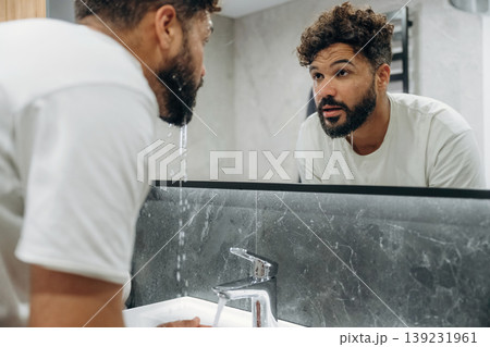 Washes face. Guy is in the bathroom, taking care of his appearance Washes face. Guy is in the bathroom, taking care of his appearance 139231961