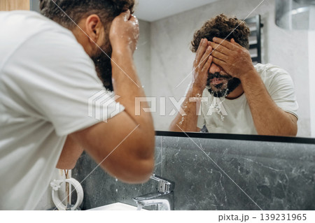 Washes face. Guy is in the bathroom, taking care of his appearance Washes face. Guy is in the bathroom, taking care of his appearance 139231965