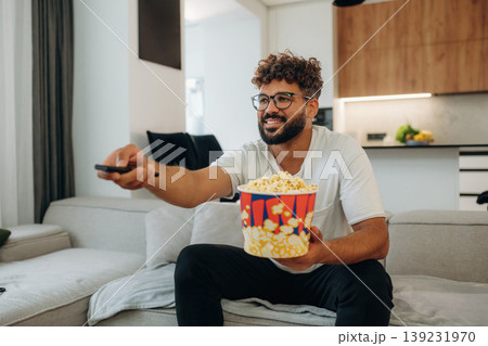 Popcorn and TV controller. Man is in the modern domestic room at home 139231970