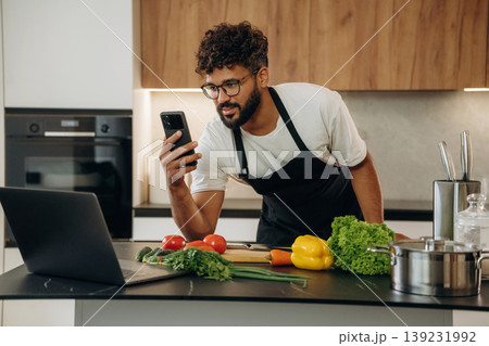 Smartphone is in hand. Handsome man is preparing food on the kitchen Smartphone is in hand. Handsome man is preparing food on the kitchen 139231992