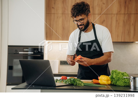 Slicing the vegetables. Handsome man is preparing food on the kitchen Slicing the vegetables. Handsome man is preparing food on the kitchen 139231998