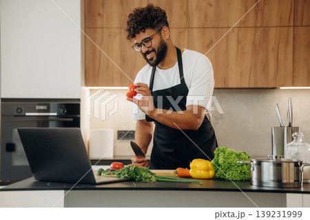 Slicing the vegetables. Handsome man is preparing food on the kitchen Slicing the vegetables. Handsome man is preparing food on the kitchen 139231999