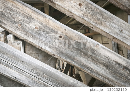 Close-up of weathered wooden beams arranged diagonally, showing aged texture, cracks, and rustic character of an old structure. 139232130
