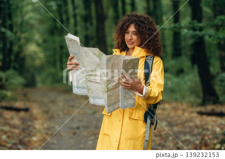 Paper map is in hands, looking at location. Young woman enjoying nature in the forest under the rain 139232153