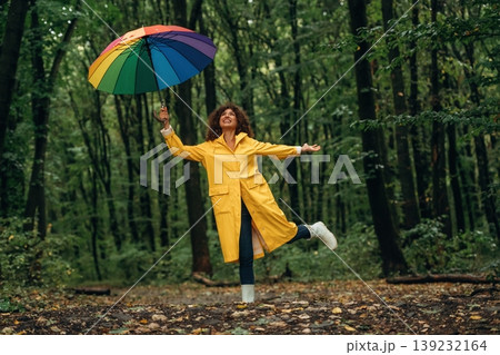 Running with colorful umbrella. Young woman enjoying nature in the forest under the rain Running with colorful umbrella. Young woman enjoying nature in the forest under the rain 139232164