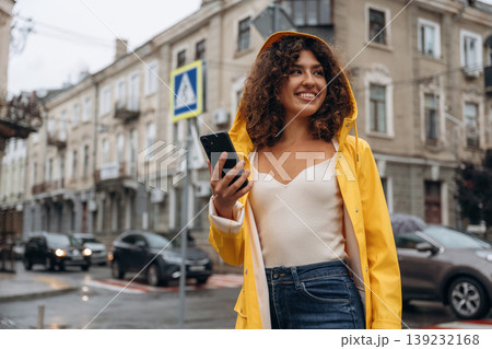 Black colored smartphone, standing. Happy young woman in the city during the rain Black colored smartphone, standing. Happy young woman in the city during the rain 139232168