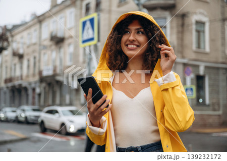 Texting by using smartphone. Happy young woman in the city during the rain Texting by using smartphone. Happy young woman in the city during the rain 139232172