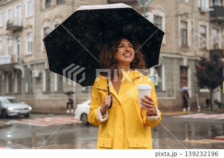 Hot drink is in the paper cup. Happy young woman in the city during the rain 139232196