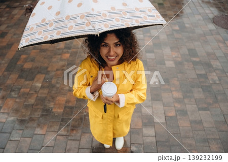 Top view of woman that is standing with an umbrella and a cup of coffee in a rainy city, on the cobblestones 139232199