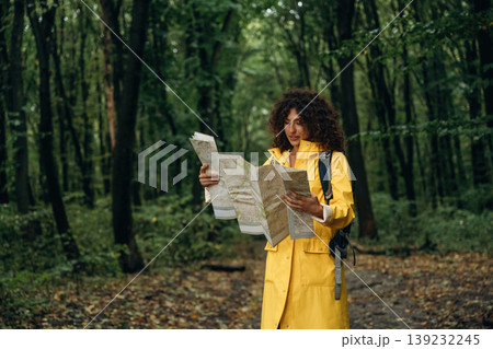 Paper map is in hands, looking at location. Young woman enjoying nature in the forest under the rain Paper map is in hands, looking at location. Young woman enjoying nature in the forest under the rain 139232245