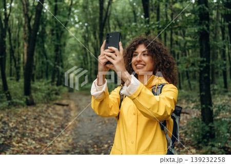 Making photos by using smartphone. Young woman enjoying nature in the forest under the rain 139232258