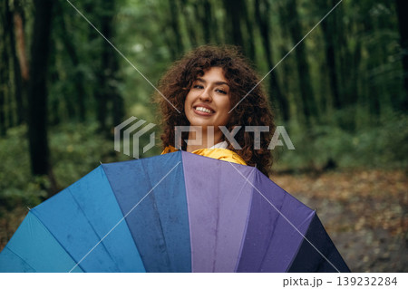 Posing, standing and holding colorful umbrella. Young woman enjoying nature in the forest under the rain Posing, standing and holding colorful umbrella. Young woman enjoying nature in the forest under the rain 139232284