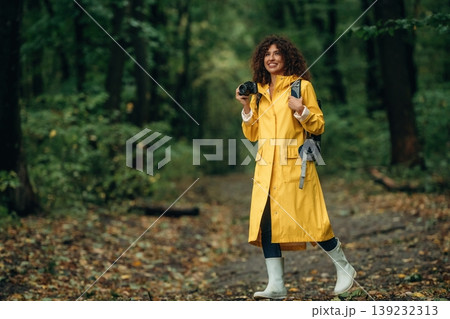 Photographer is with camera. Young woman enjoying nature in the forest under the rain Photographer is with camera. Young woman enjoying nature in the forest under the rain 139232313
