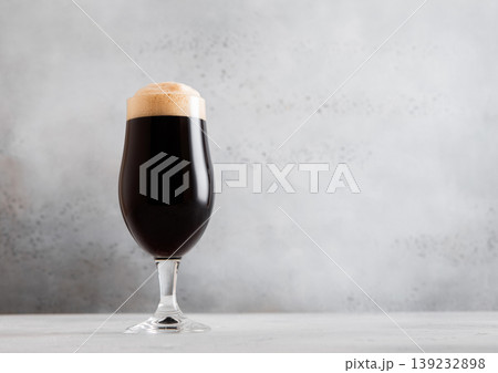 Glass of fresh cold dark stout beer with foam on light table background. 139232898
