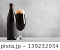 Bottle and glass of fresh cold dark stout beer with foam on light table background. 139232934