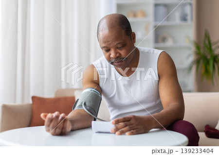 Mature African American man using blood pressure monitor on arm at home 139233404