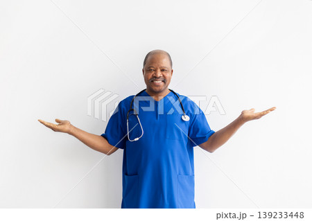 Friendly black male doctor in blue scrubs gesturing with both open hands Friendly black male doctor in blue scrubs gesturing with both open hands 139233448